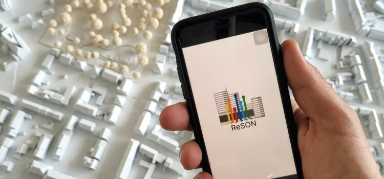 Smartphone mit App Logo vor einem Stadtmodell
